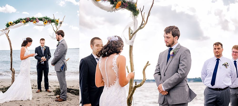 A beachside wedding ceremony taking place under a floral arch with waves and clouds in the background.