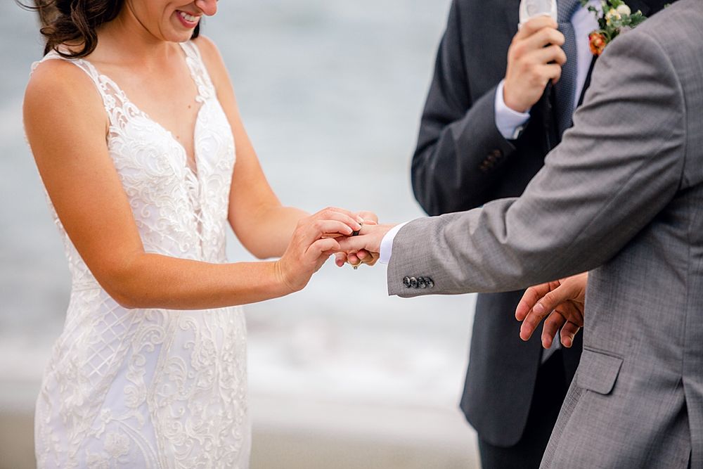 Close-up of hands during a wedding ring exchange ceremony showing lace dress and gray suit details.