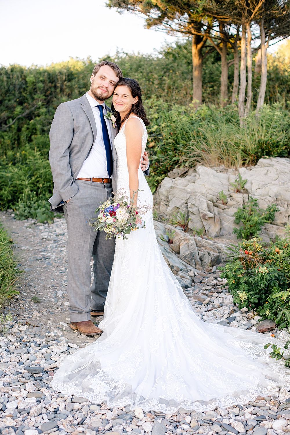 A wedding portrait on a rocky path with a flowing white dress train and natural forest backdrop.