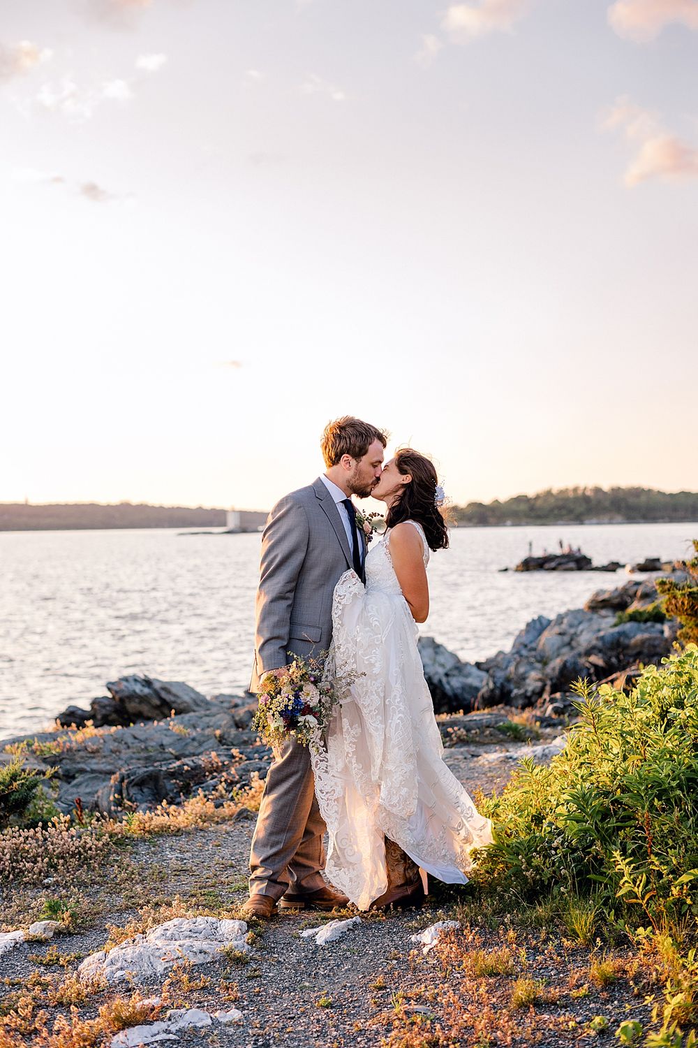 Wedding couple shares intimate moment on coastal rocks during golden hour sunset.