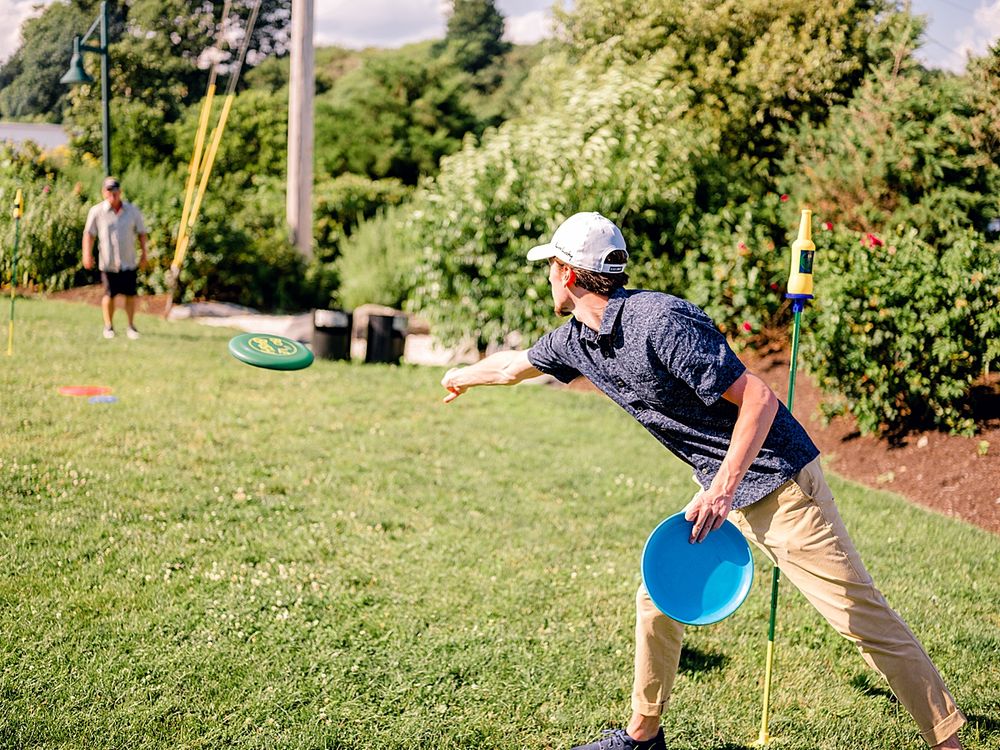 Person playing disc golf on sunny lawn throws blue frisbee.