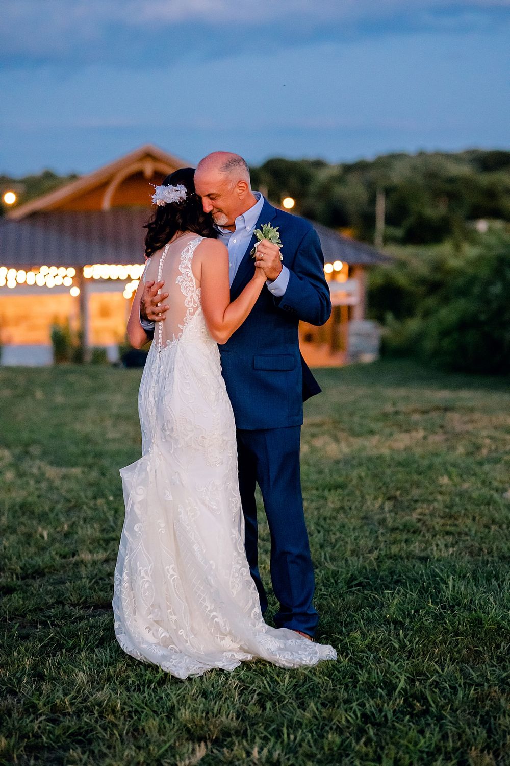 A couple shares a dance on grass during their outdoor evening wedding reception.