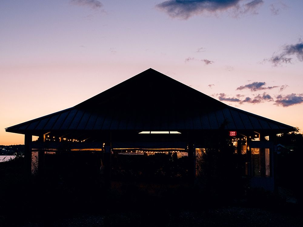 Silhouette of a pavilion against a purple sunset sky with string lights.