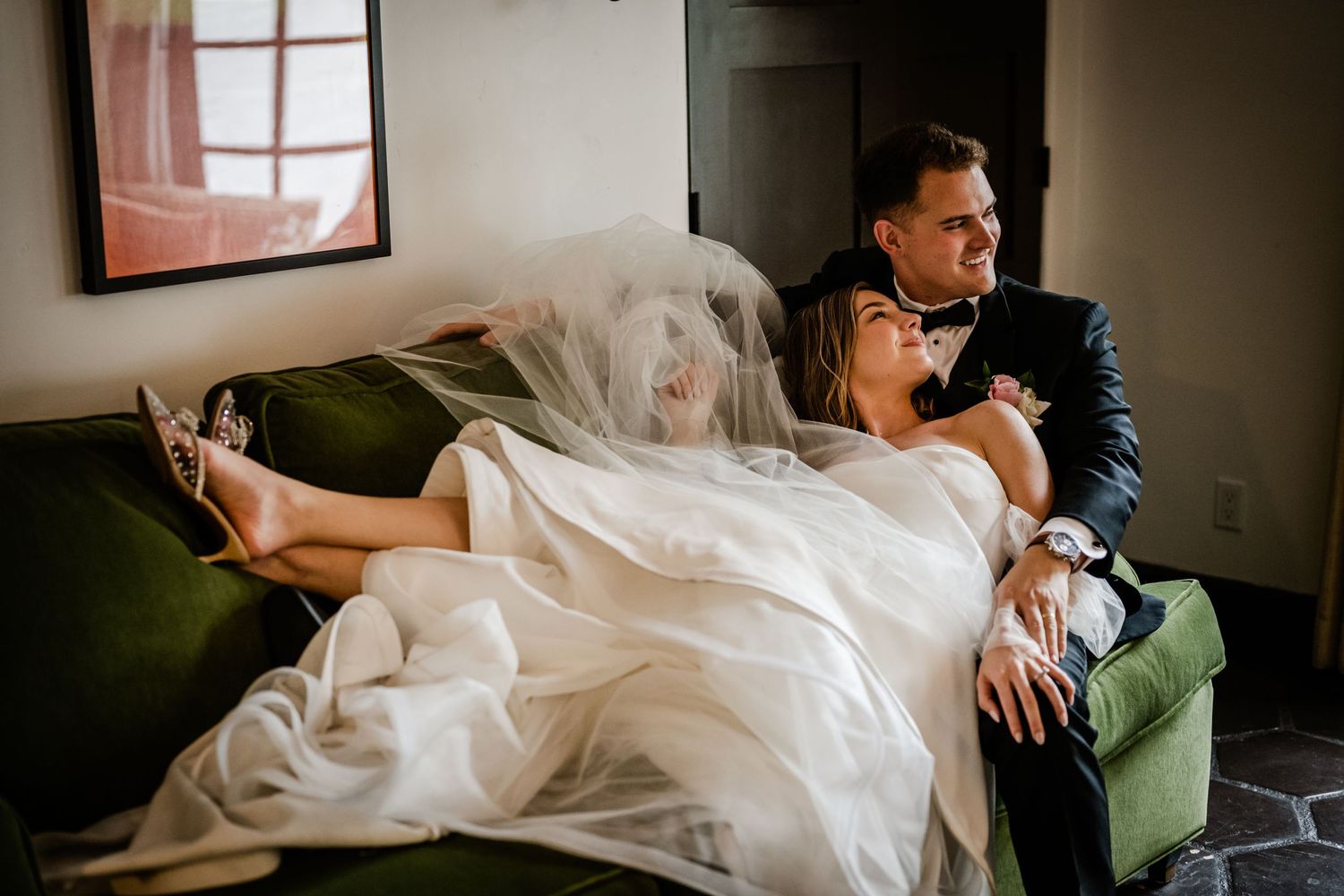 Couple relaxing on a green velvet couch in formal attire.