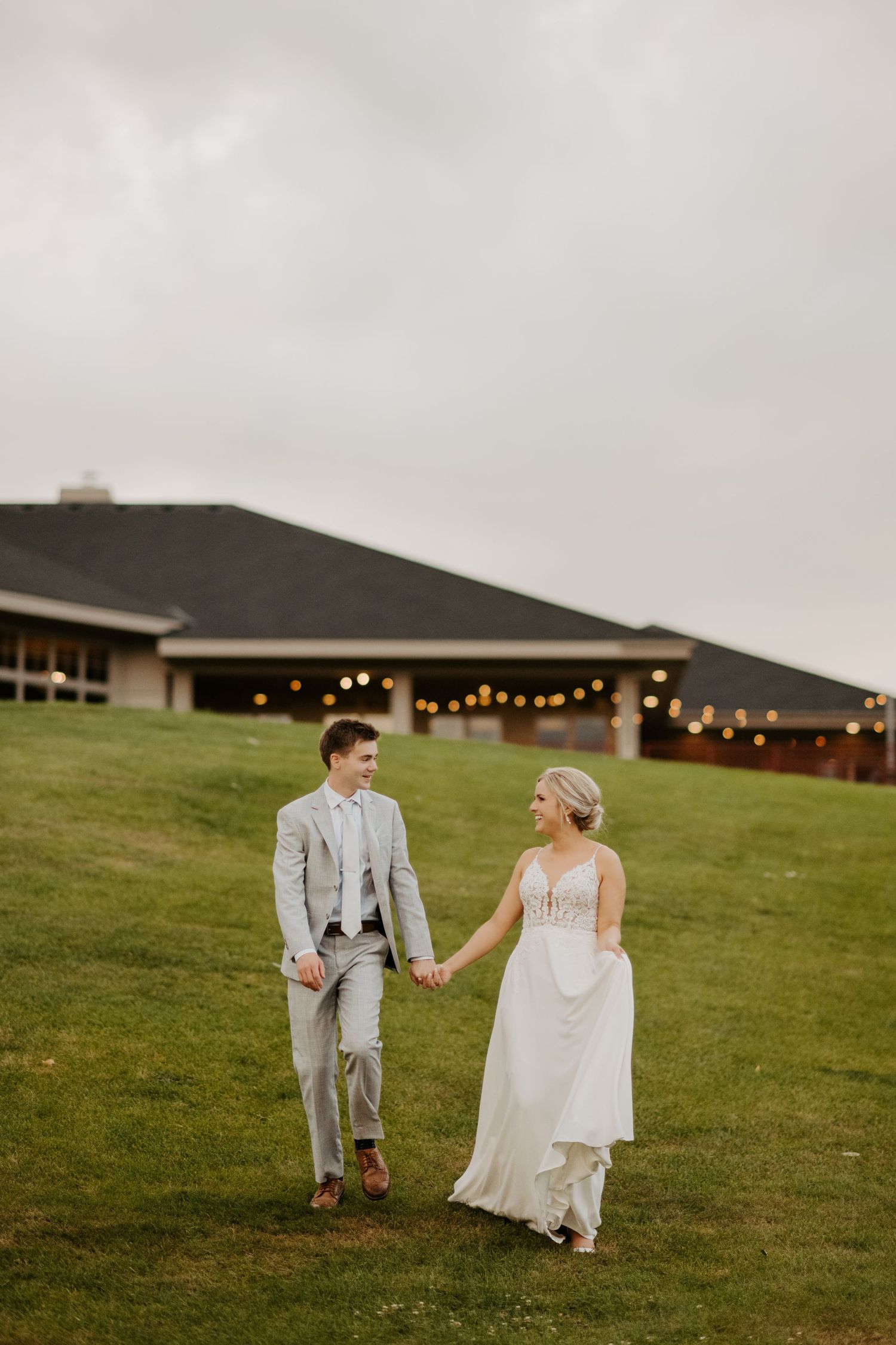 A bride and groom walk hand in hand in front of their wedding venue