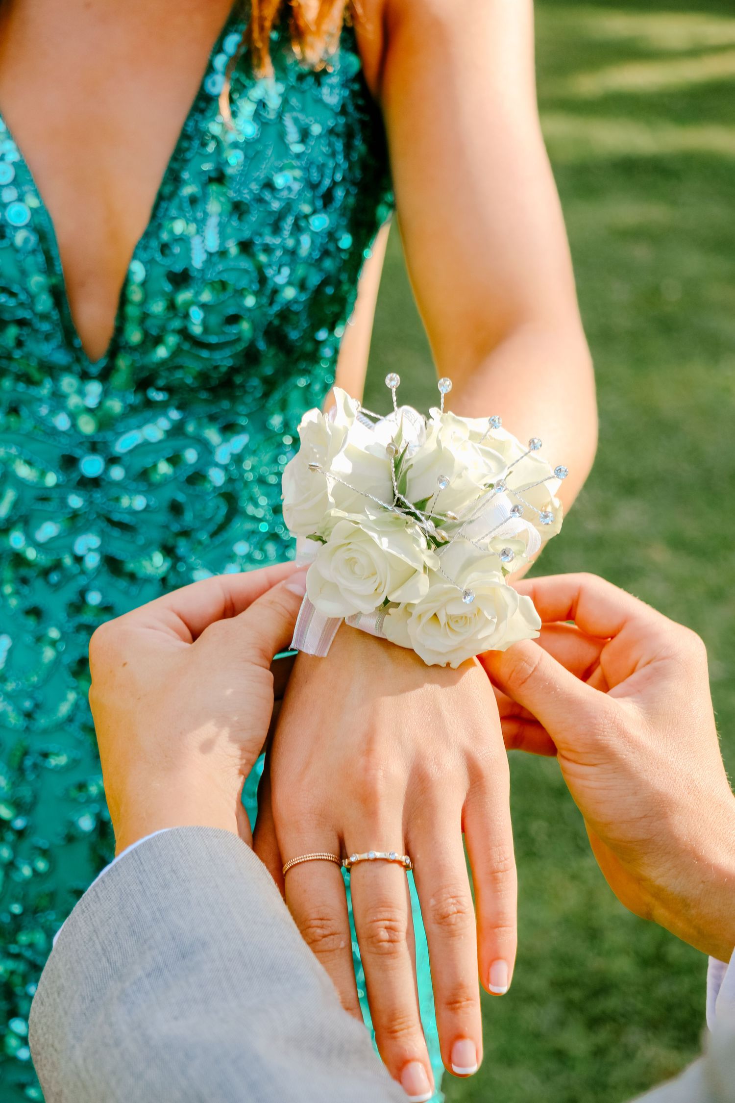 Hands placing a delicate white flower corsage on a wrist against a sparkly turquoise dress.