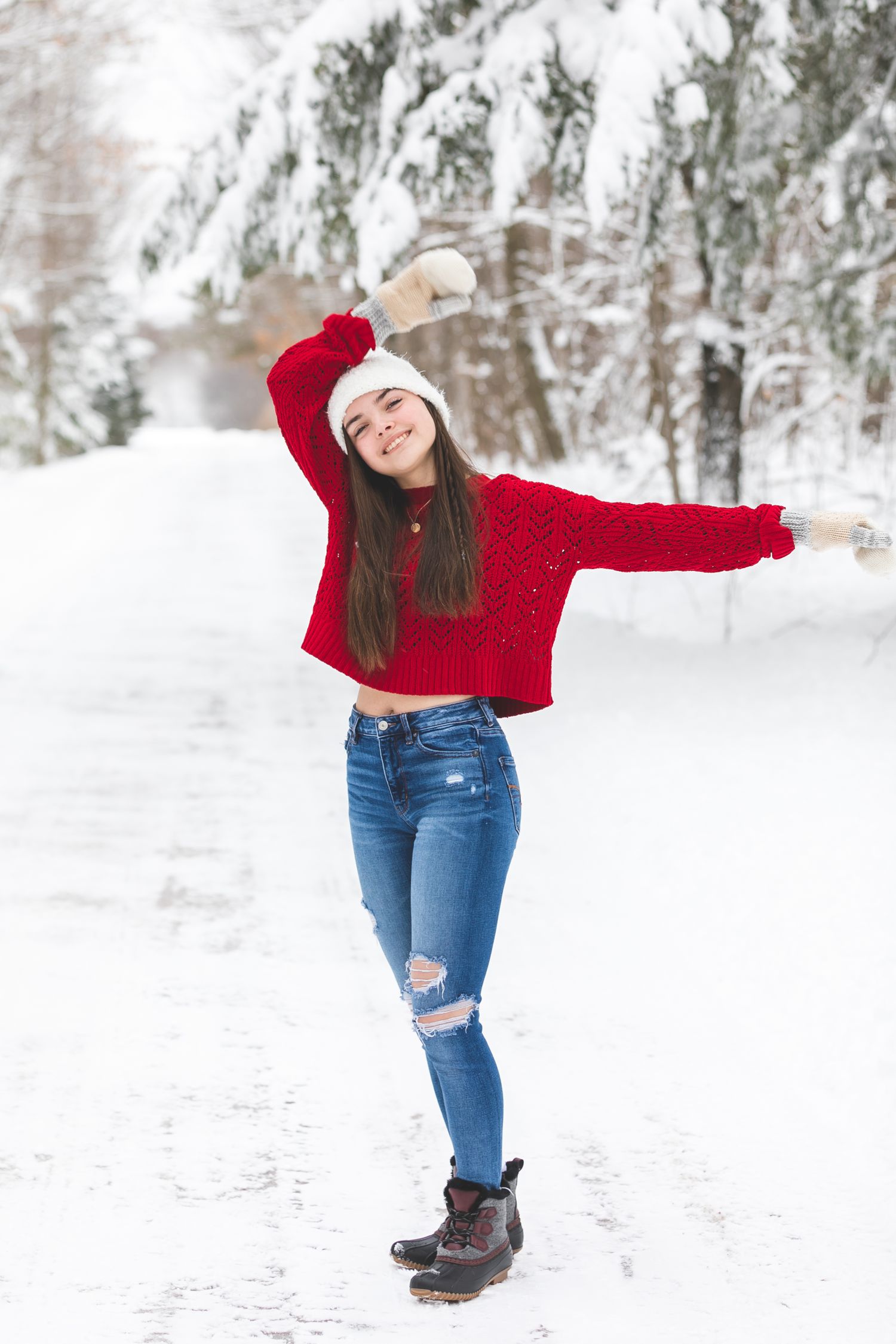 Person in red sweater and jeans plays in snowy winter landscape with snow-covered trees.