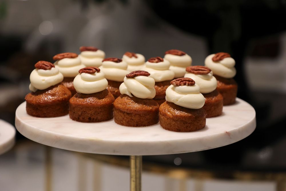 Mini chocolate cupcakes with cream frosting and red garnish displayed on a white cake stand.