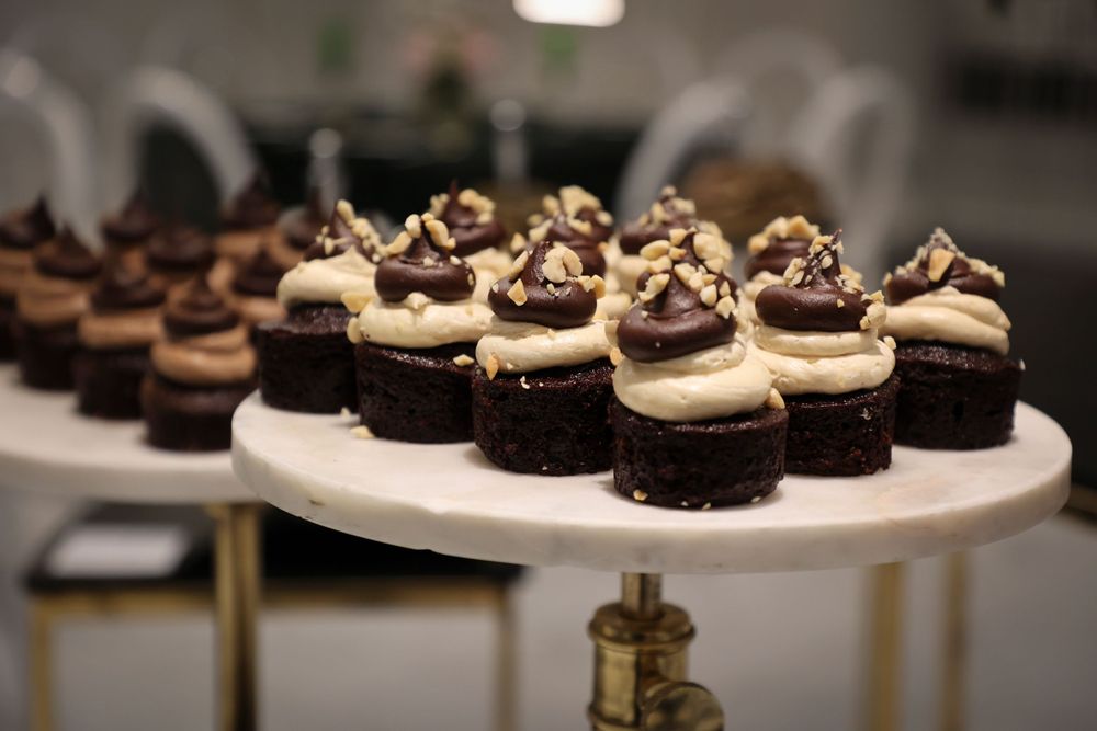 Chocolate mini cupcakes topped with vanilla frosting and chocolate shavings on a white stand.