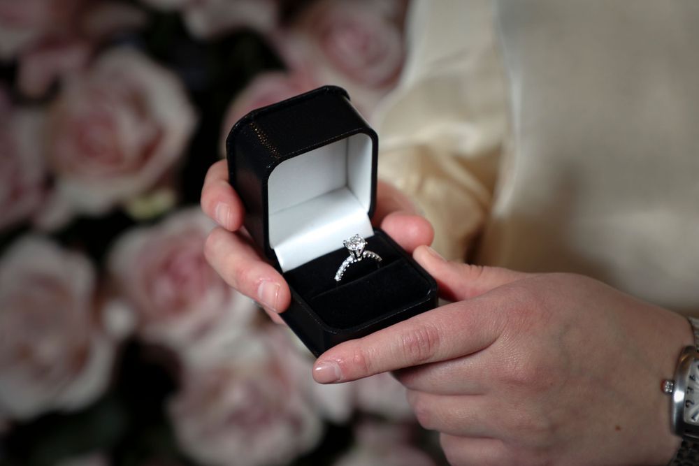 Diamond engagement ring in black velvet box with pink roses in background.