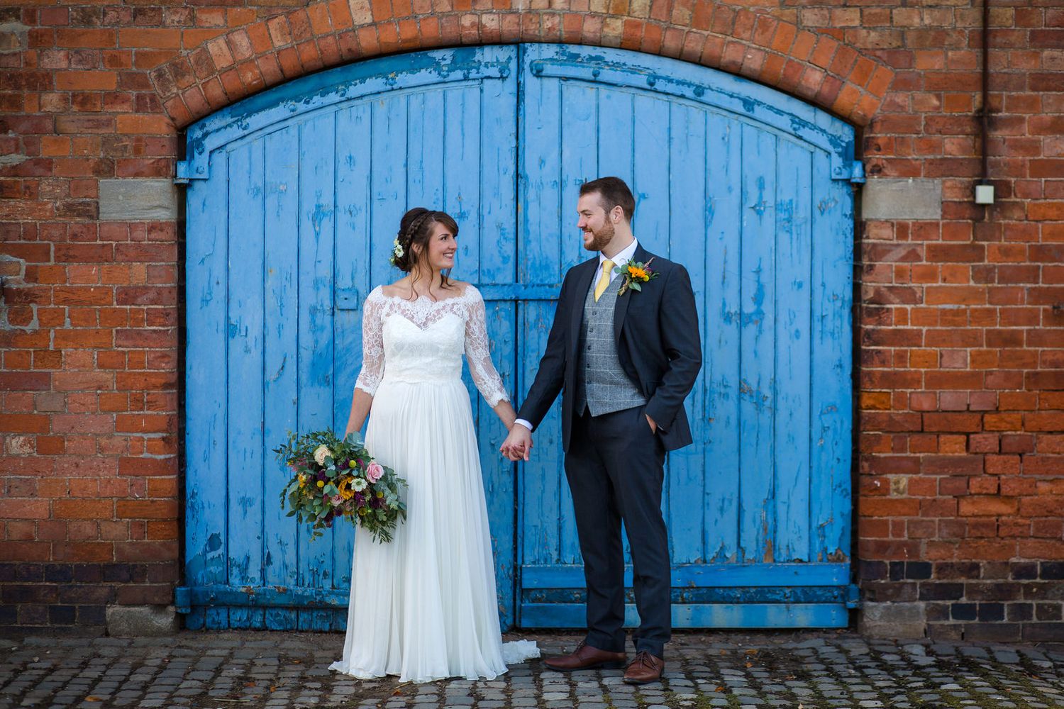 Bride & Groom holding hands in front of blue doors at Thorpe Garden wedding venue