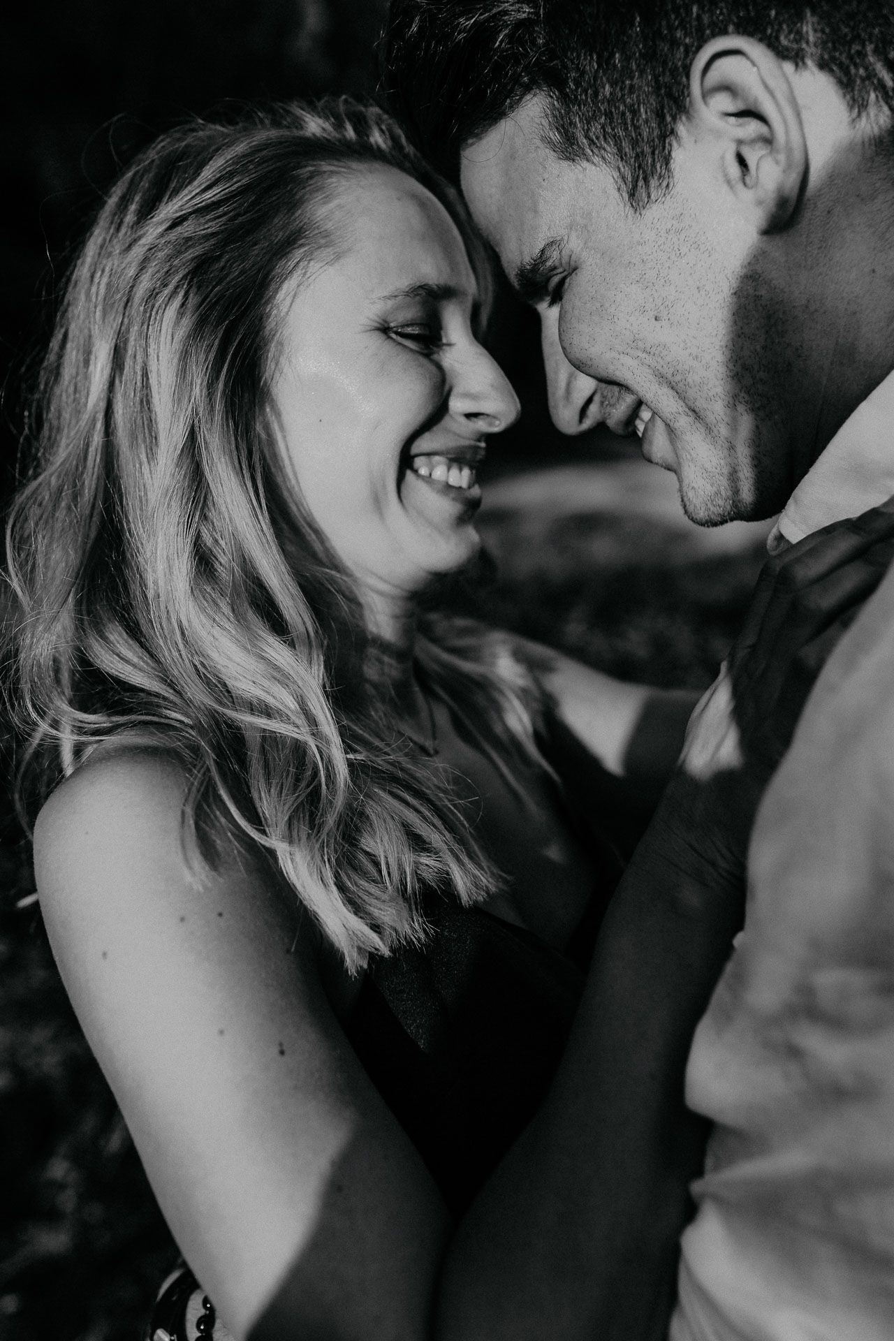 An intimate black and white portrait of a couple sharing a close moment outdoors.