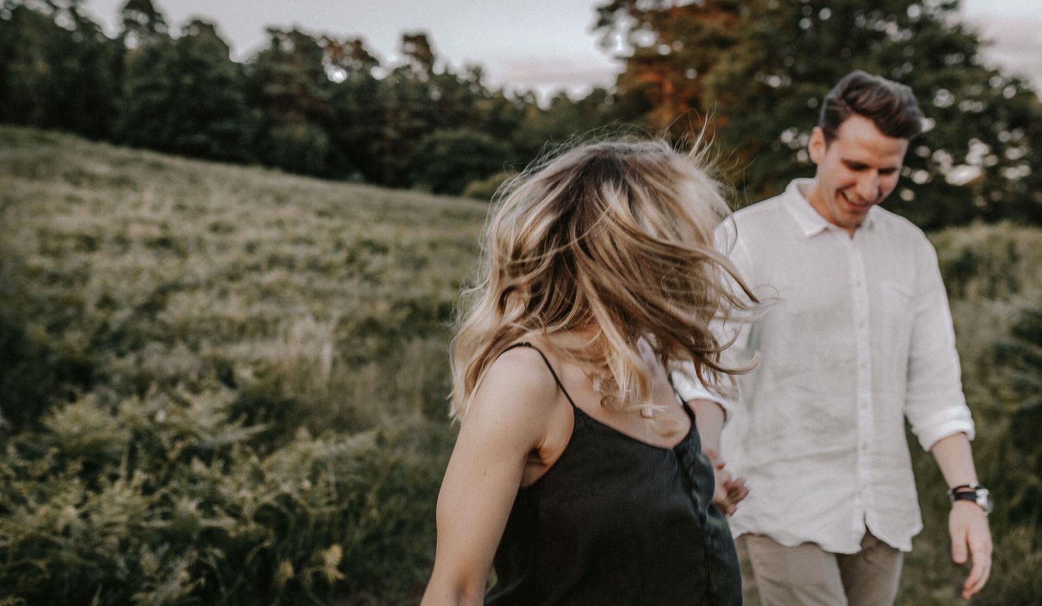 A couple walks through a meadow during golden hour with sunlight illuminating the scene.