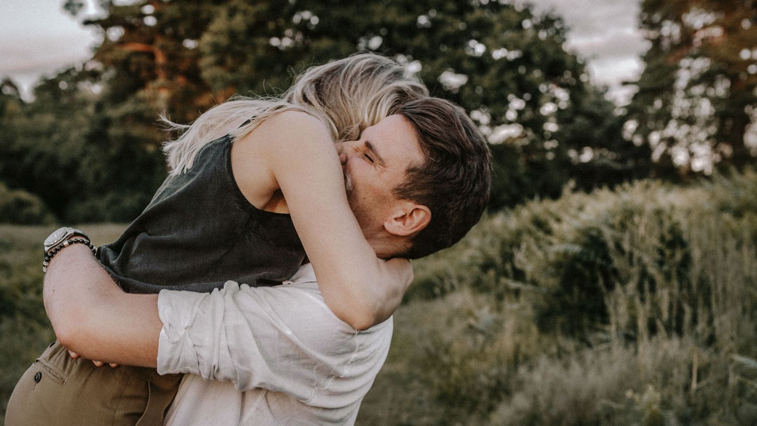 A romantic embrace captured in soft evening light amidst natural surroundings.