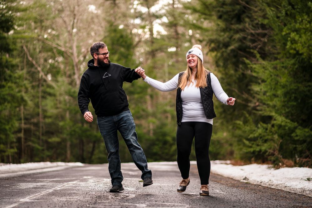 Candid engagement photos on a winding forest path with patches of snow.