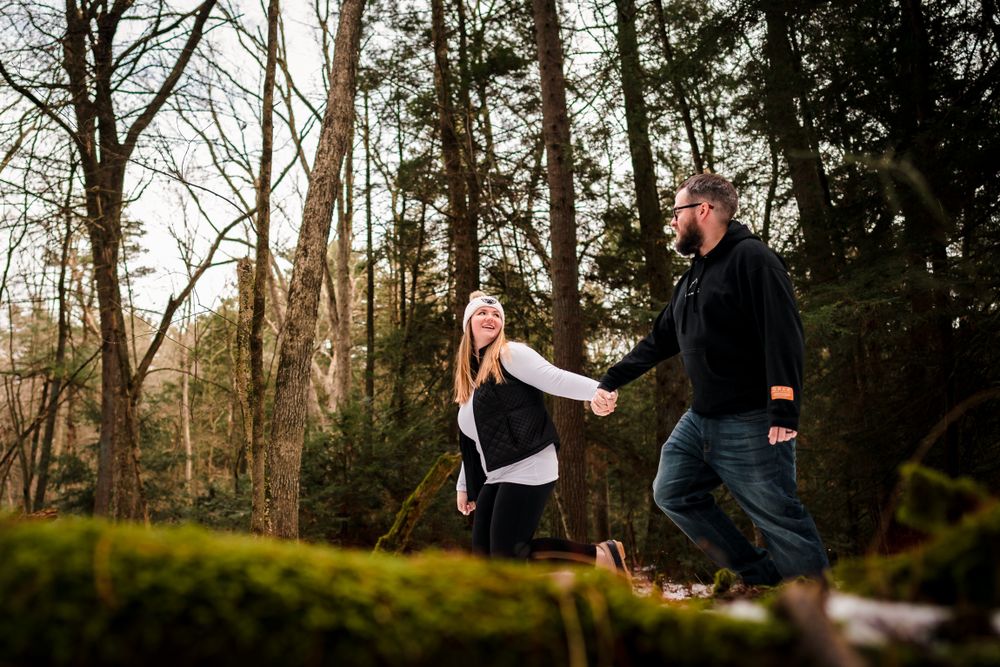 Couple shares tender moments together during winter forest engagement photoshoot with snow-covered ground.