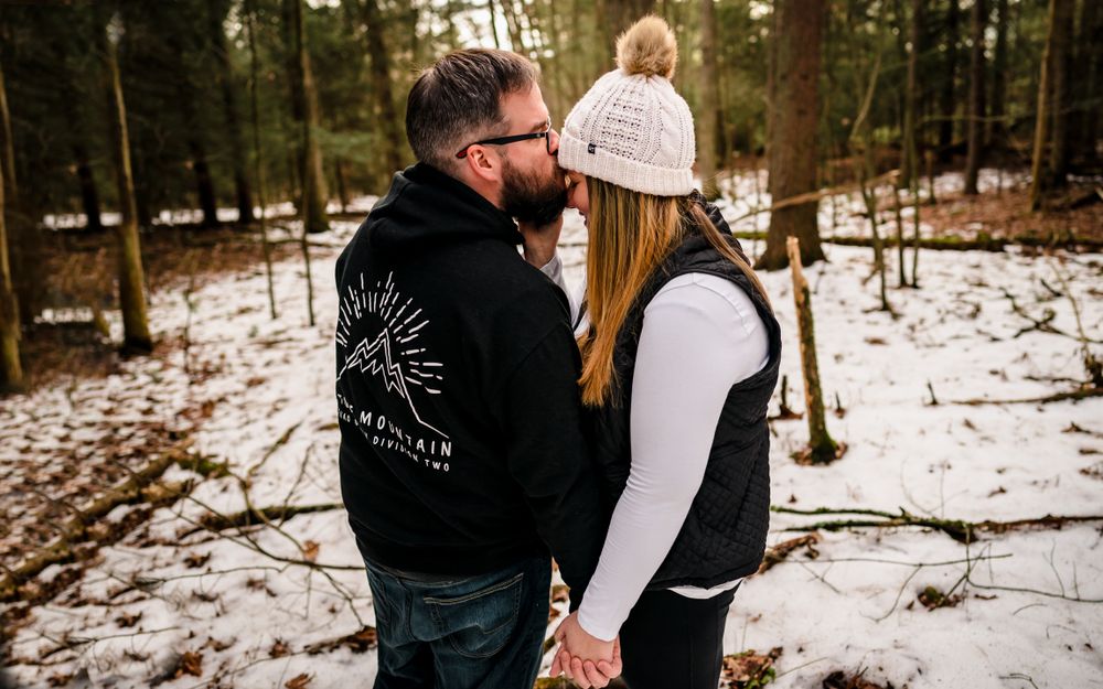Romantic winter engagement photos captured in a snowy forest setting with intimate poses and warm winter attire.