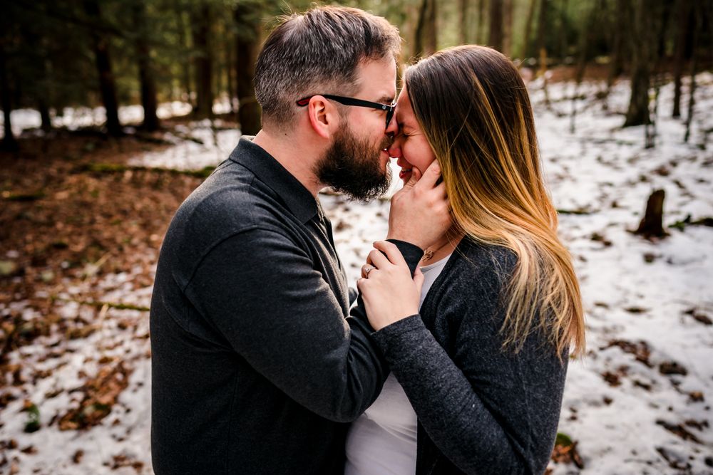 Intimate winter engagement portraits showing tender moments between couple in snowy forest setting.