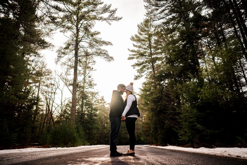Wide landscape shots of couple's engagement session in winter pine forest with dramatic lighting.
