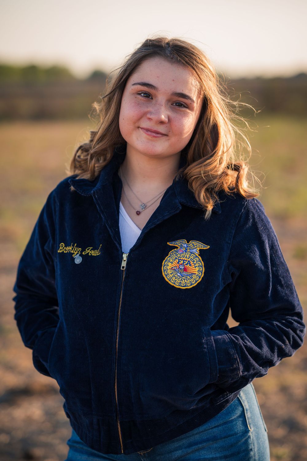 Young person in FFA jacket poses outdoors at sunset.