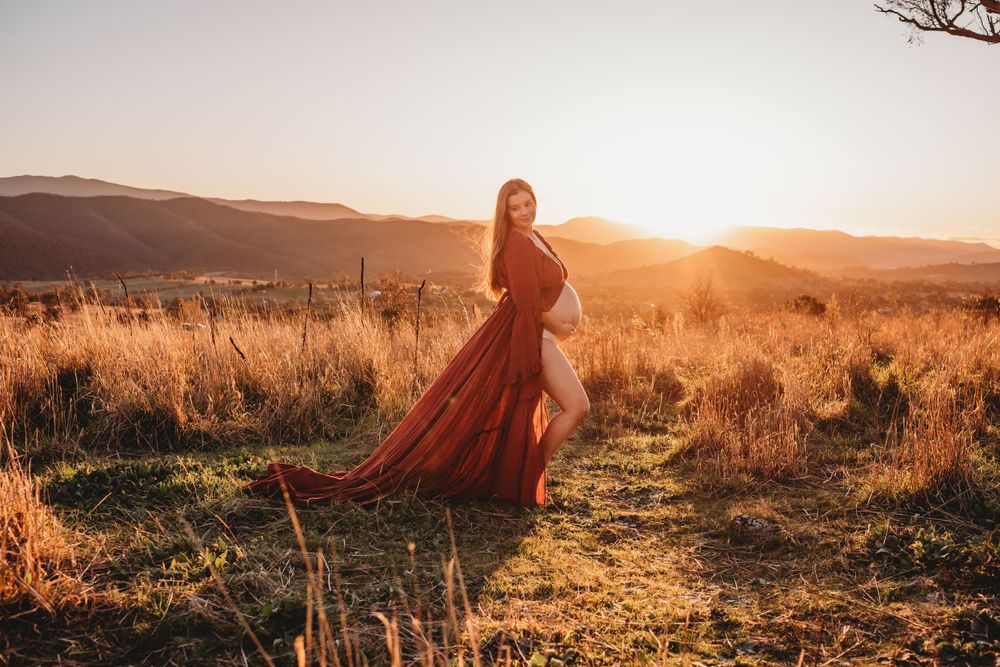 Woman in flowing red dress standing in golden sunlit field at sunset.