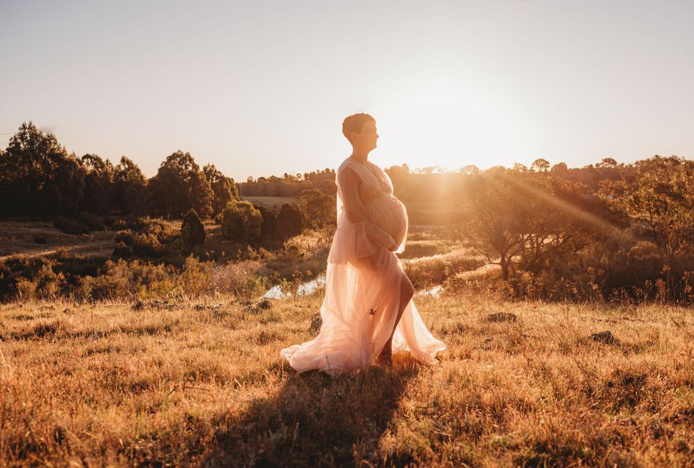 A silhouette stands in a flowing dress against a golden sunset on a hilltop.