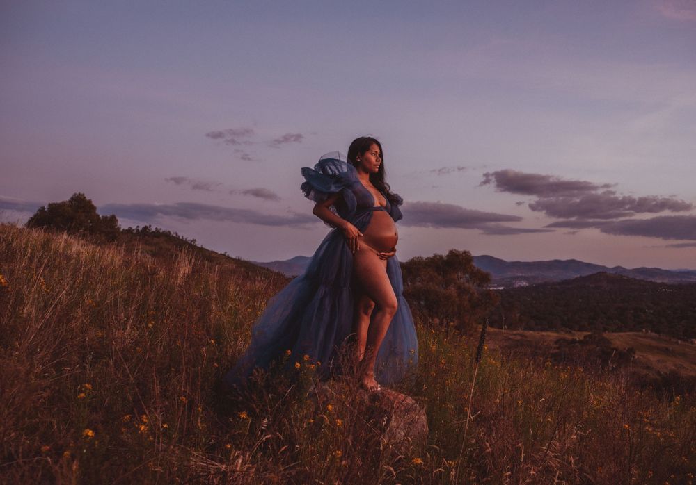 Dramatic sunset maternity portrait with flowing fabric in mountain field.