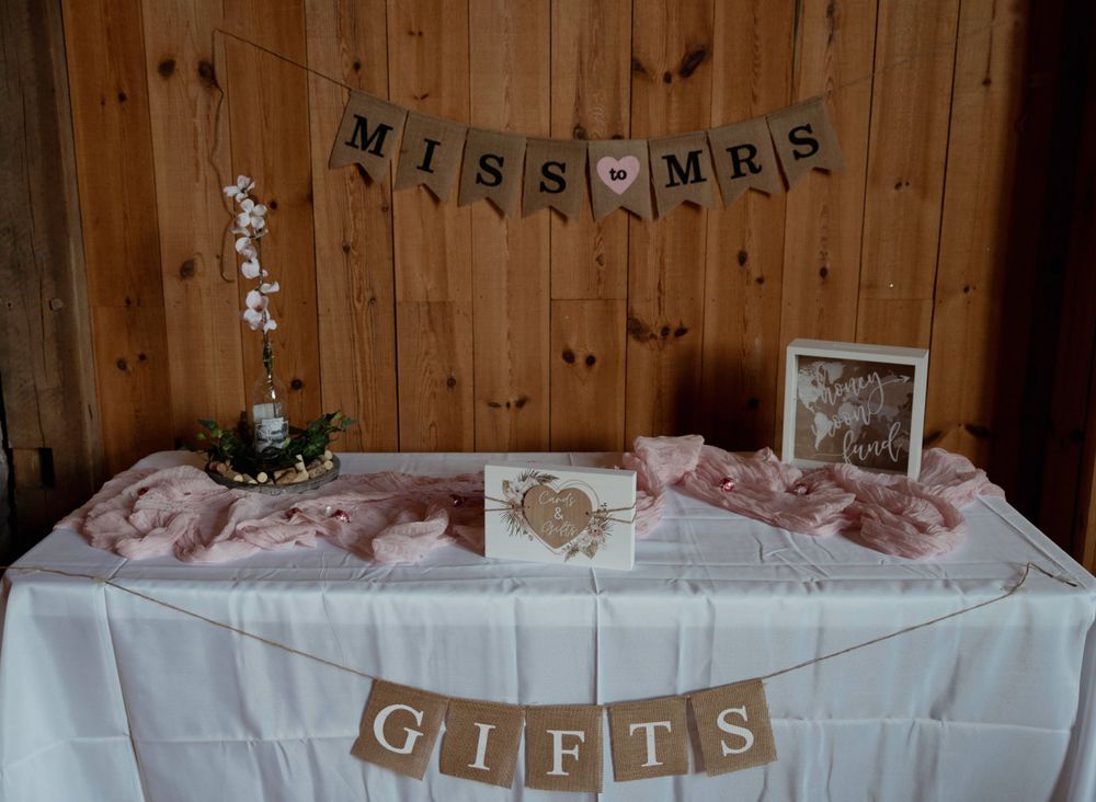 Wedding gift table with Miss Mrs and Gifts banners and pink decor on white tablecloth.