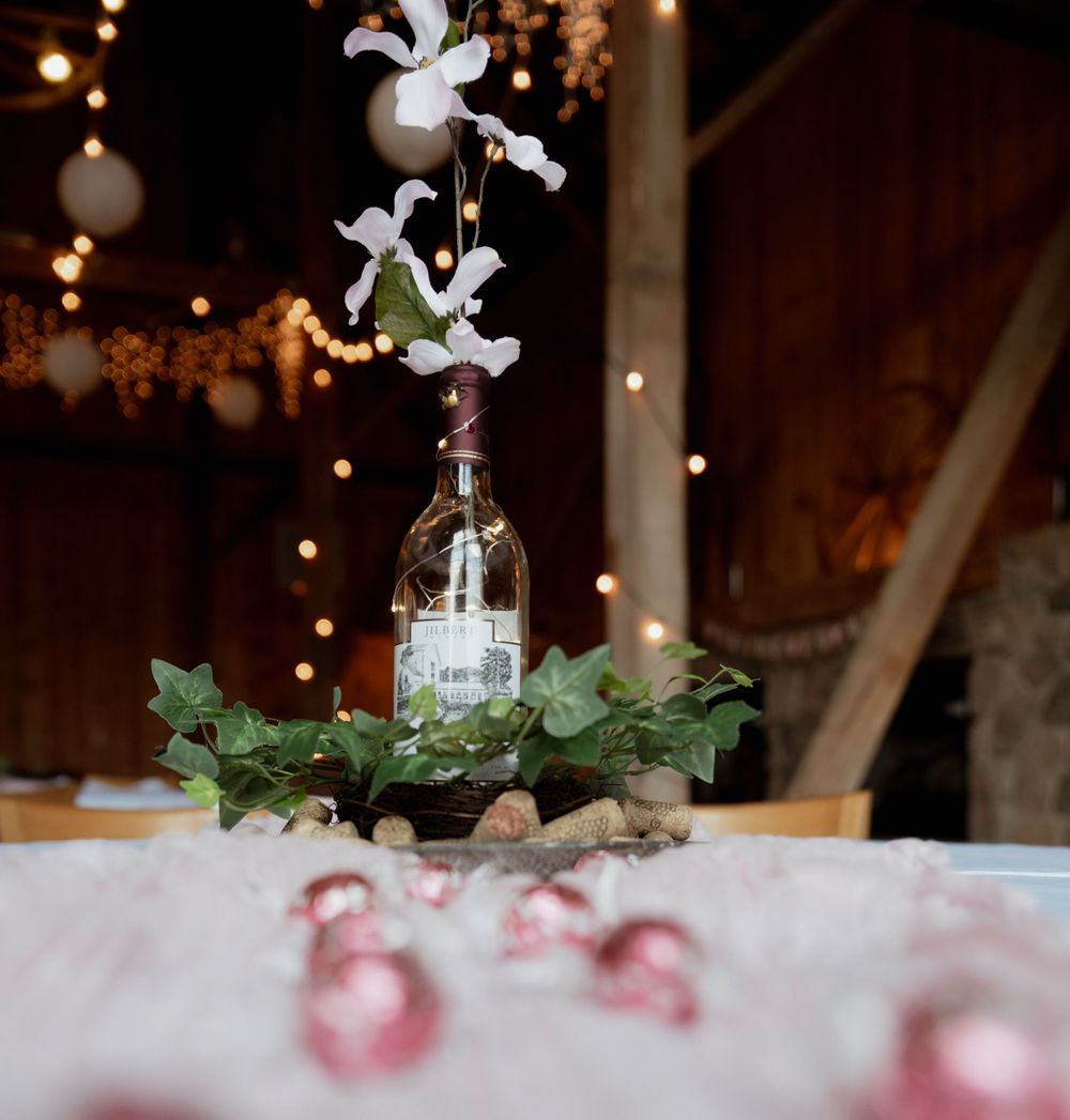 Glass bottle centerpiece with white flowers and greenery on table with twinkle lights.