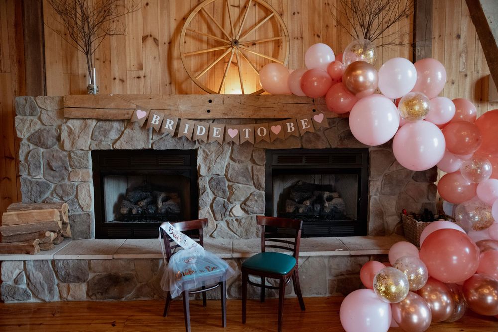 Rustic stone fireplace with wagon wheel and pink balloon arch in reception venue.