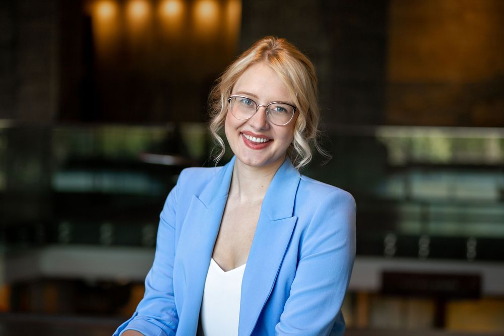 Professional portrait in a light blue blazer with warm interior lighting.
