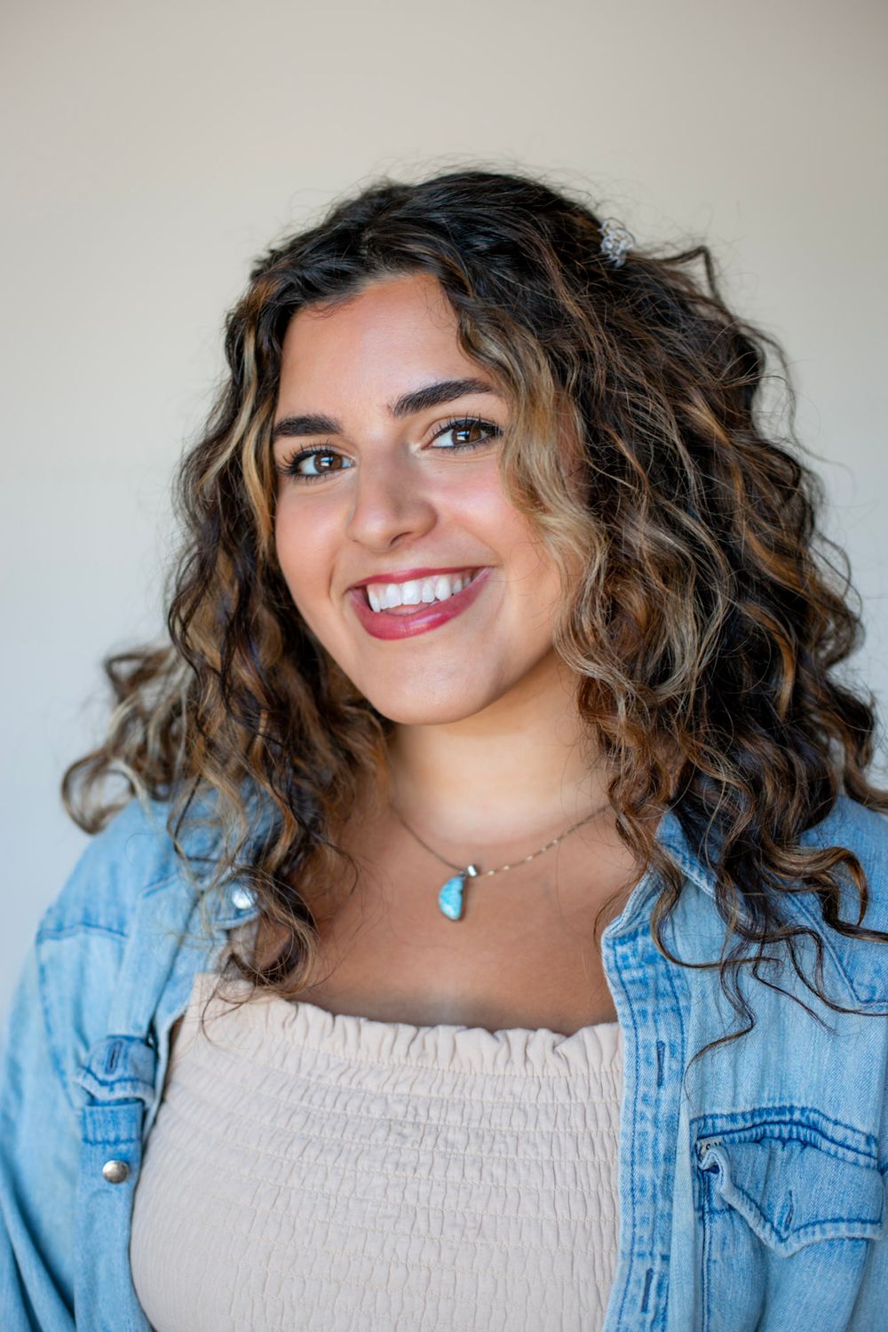 Portrait in a denim jacket and white top with a turquoise pendant necklace.