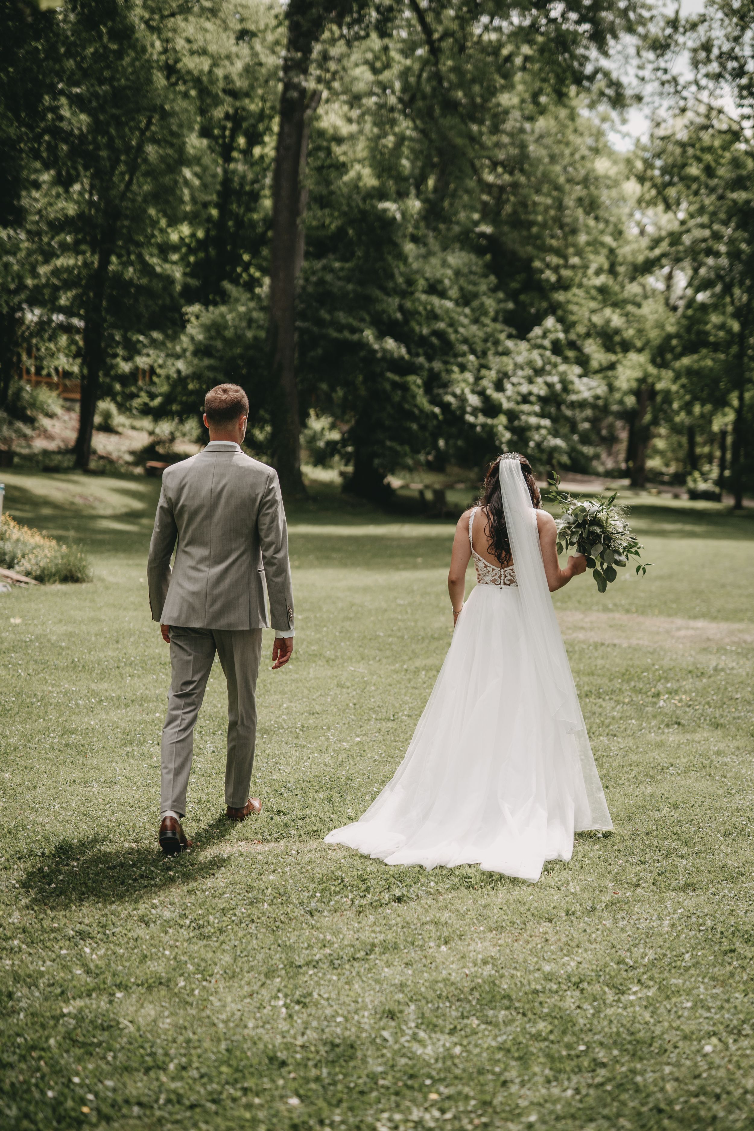 Bride and groom walking separately on lush green lawn during wedding photoshoot.
