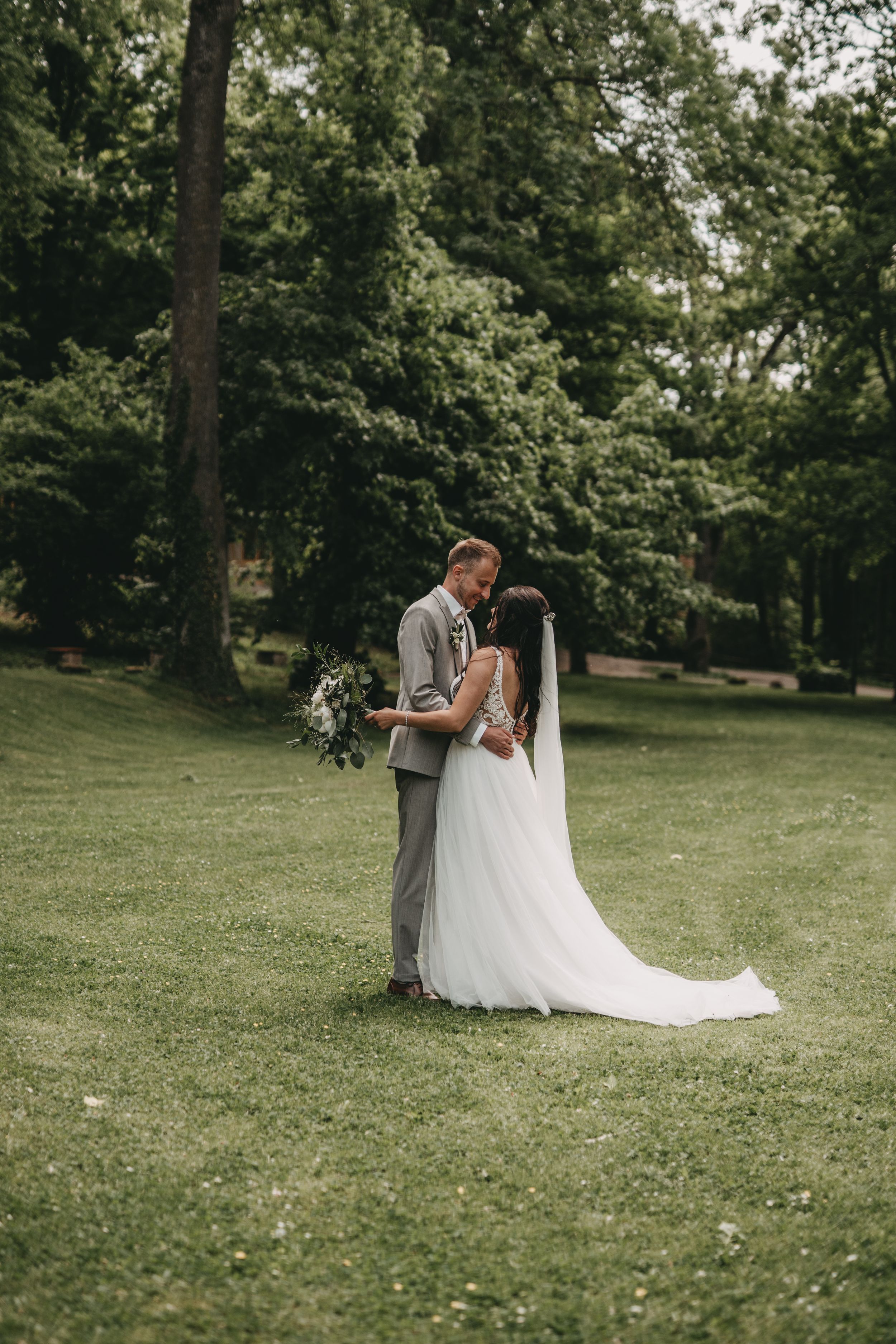 Romantic wedding couple sharing intimate moment on green lawn during outdoor photo session.