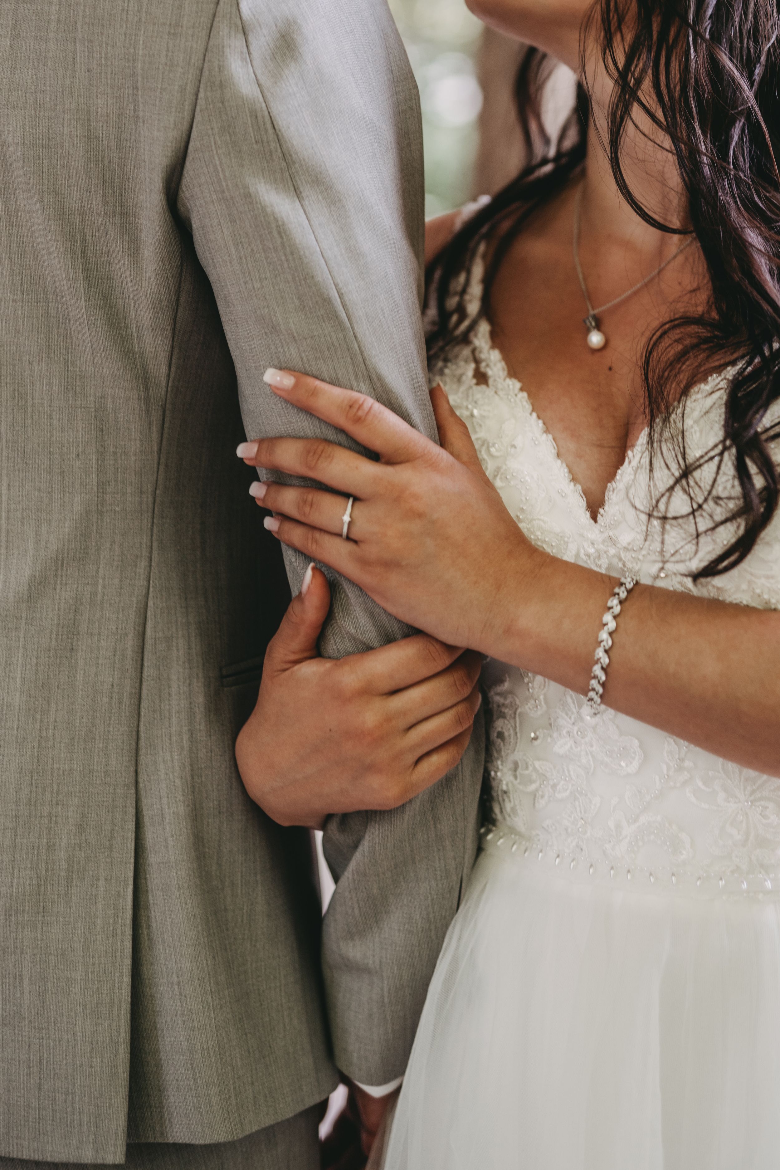 Close-up of bride's hand with wedding ring holding groom's gray suit jacket.
