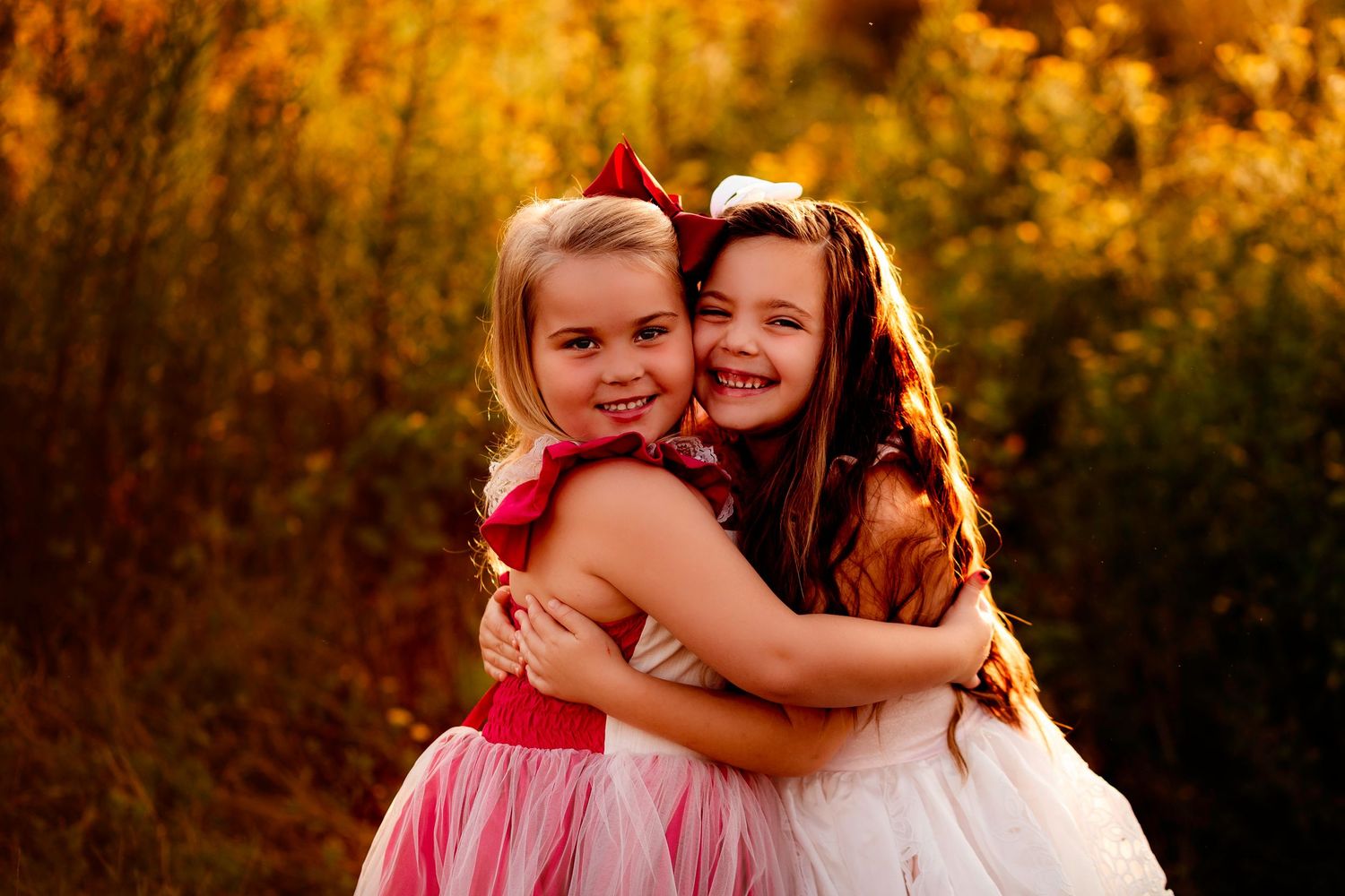 Two girls in pink and white dresses hugging and laughing during golden hour photo session.