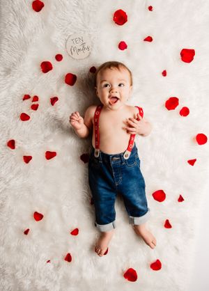 Valentine's themed photo with scattered red rose petals on white fur background.