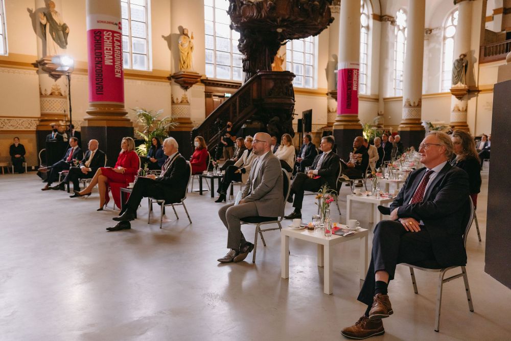 Audience seated in church interior with ornate baroque altar and columns during an event.