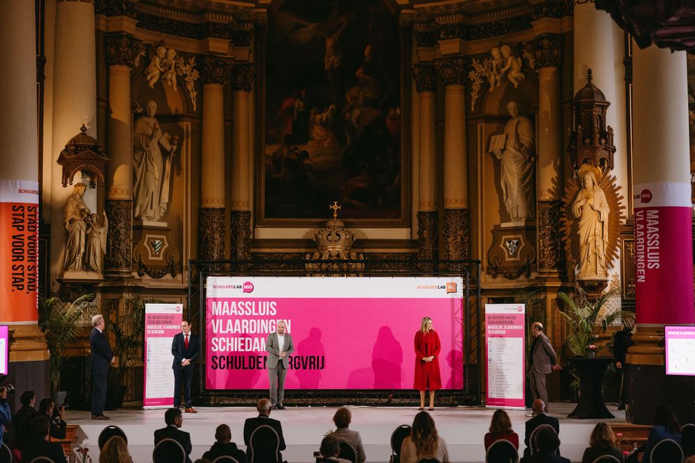 Pink-lit stage presentation against baroque church altar with audience in foreground.