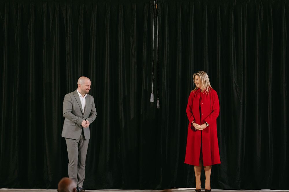Two speakers stand on stage against a black curtain backdrop during a formal presentation.