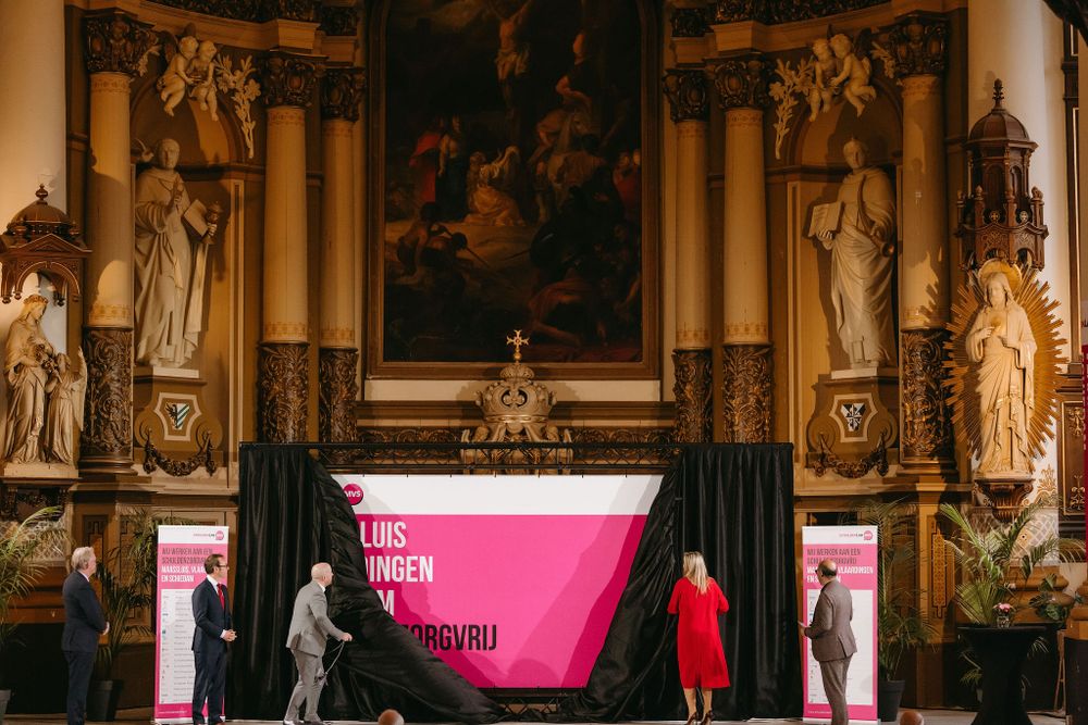 A presentation stage with pink signage set against ornate church architecture and religious statues.