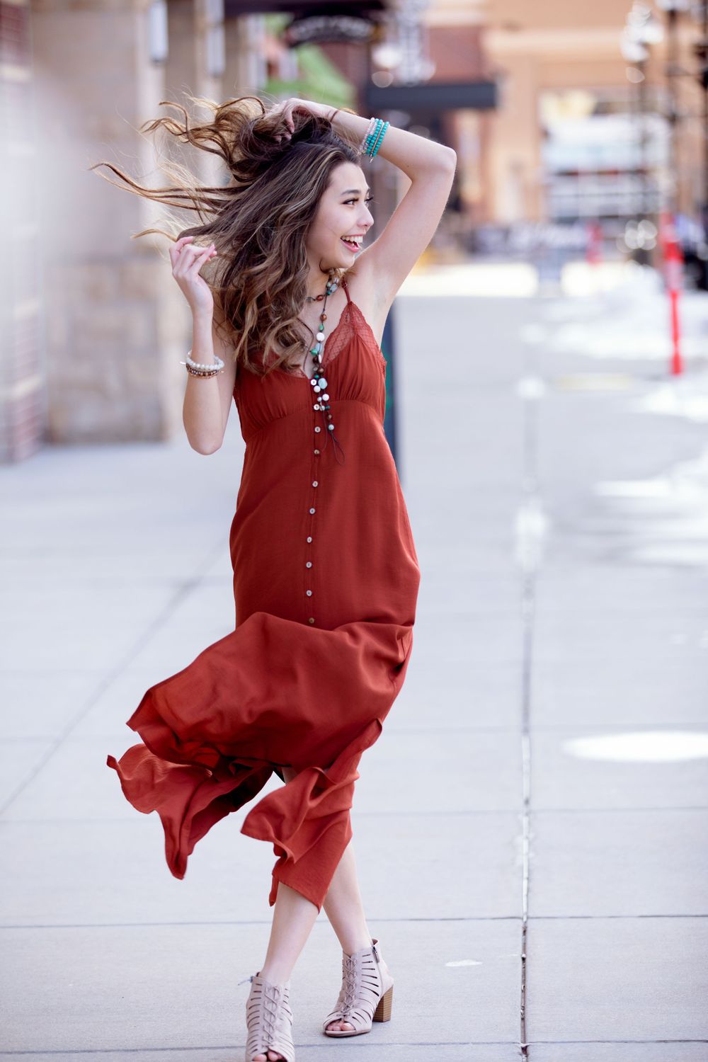 Person in flowing red dress dancing joyfully on urban sidewalk.
