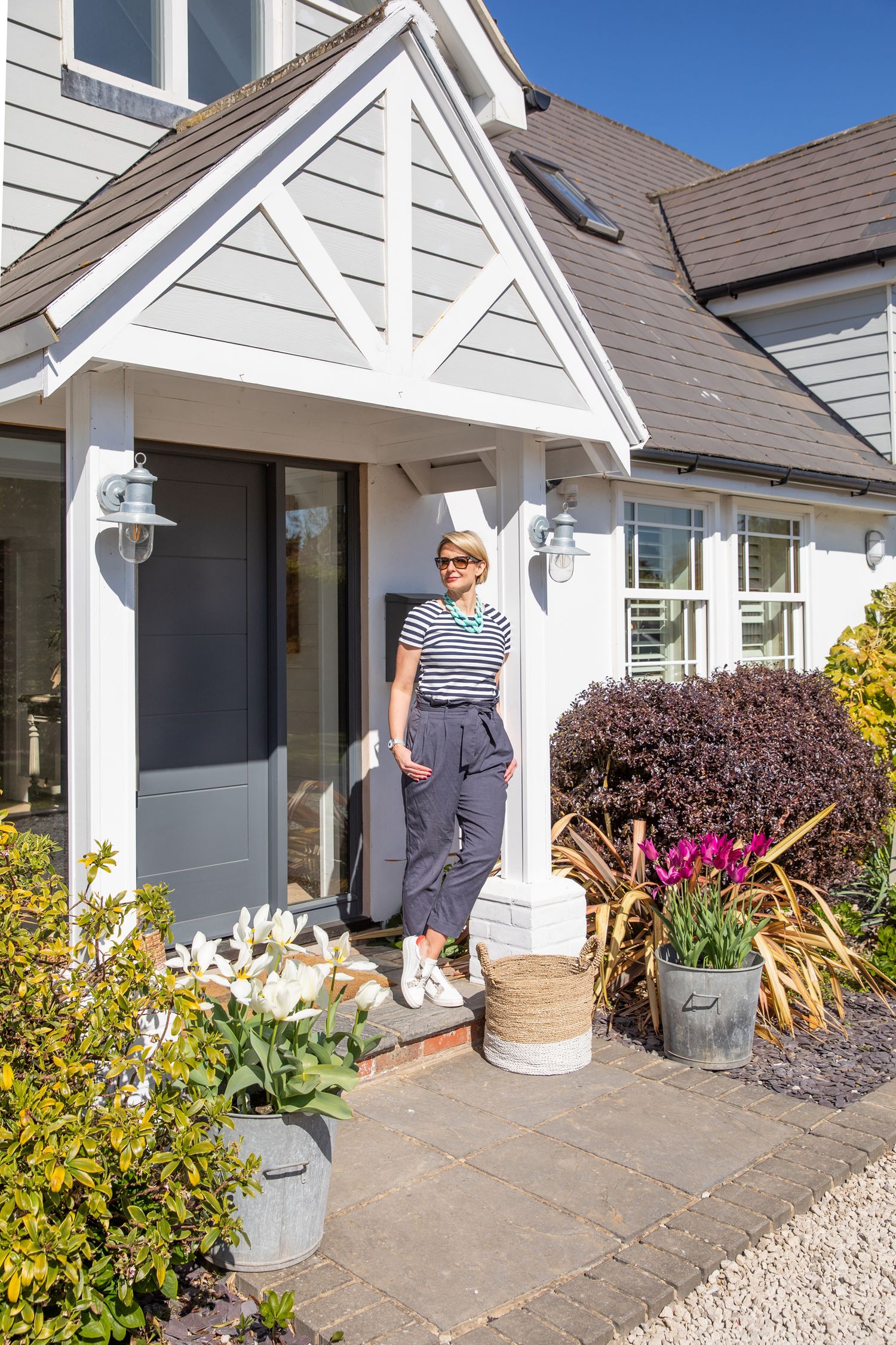 Person standing at entrance of white house with gabled porch roof and decorative landscaping during business branding photoshoot.