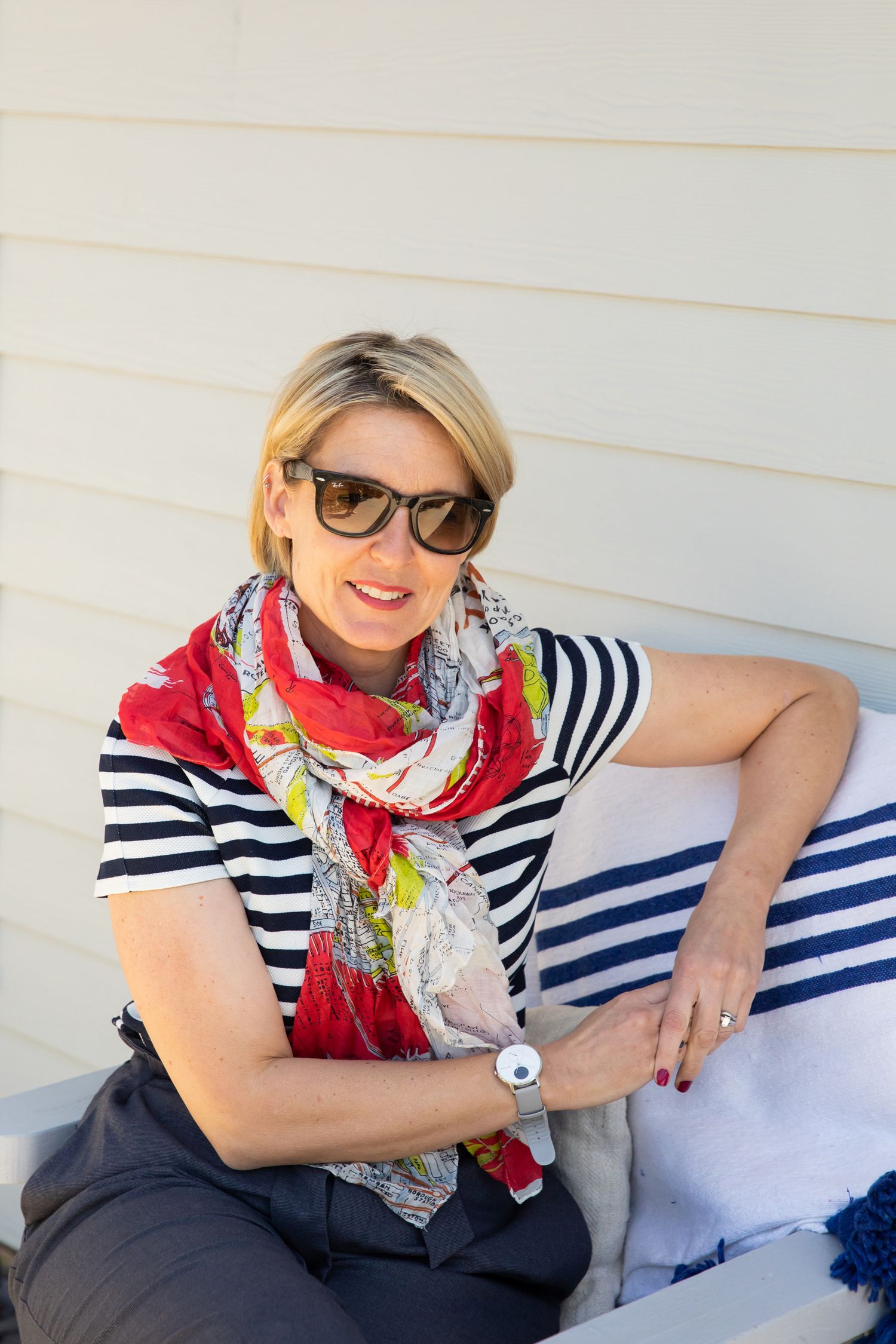 Casual outdoor portrait featuring striped shirt, red scarf, and sunglasses against white siding during business branding photoshoot.
