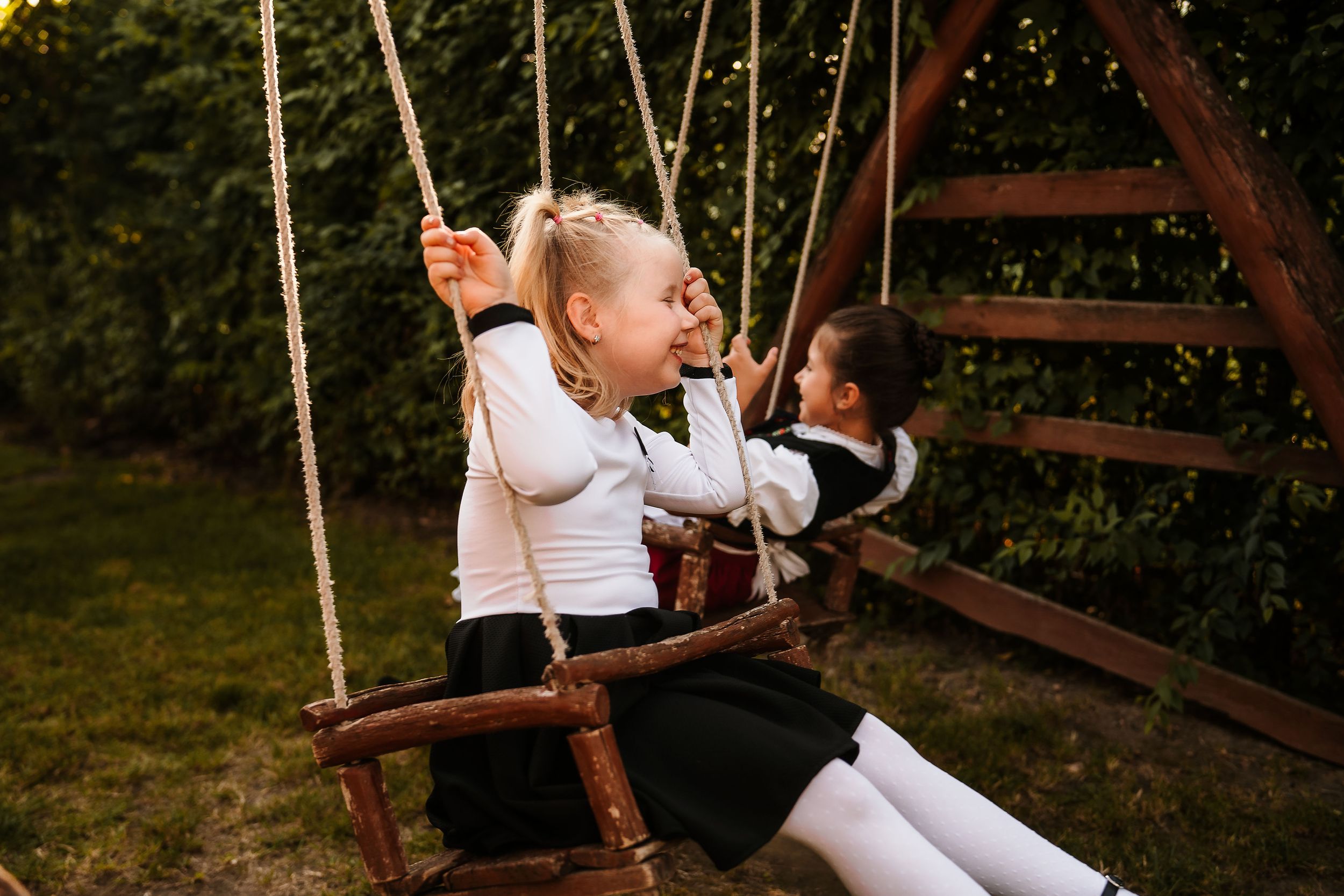 Two children enjoy playing on a wooden swing set in a backyard.