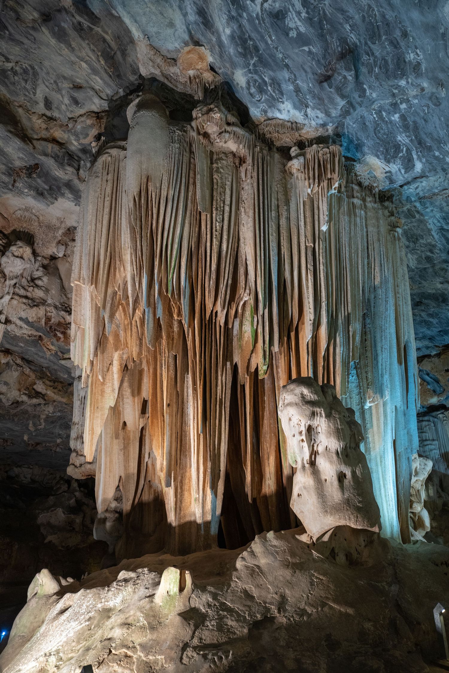 Natural cave formation with hanging stalactites illuminated by blue and amber lights.