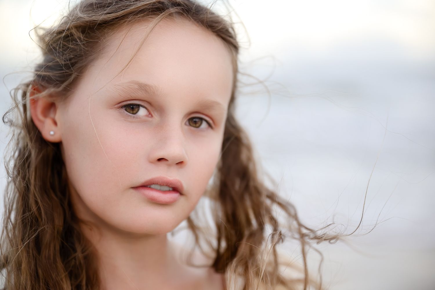 Natural light portrait of young woman with windswept brown hair.