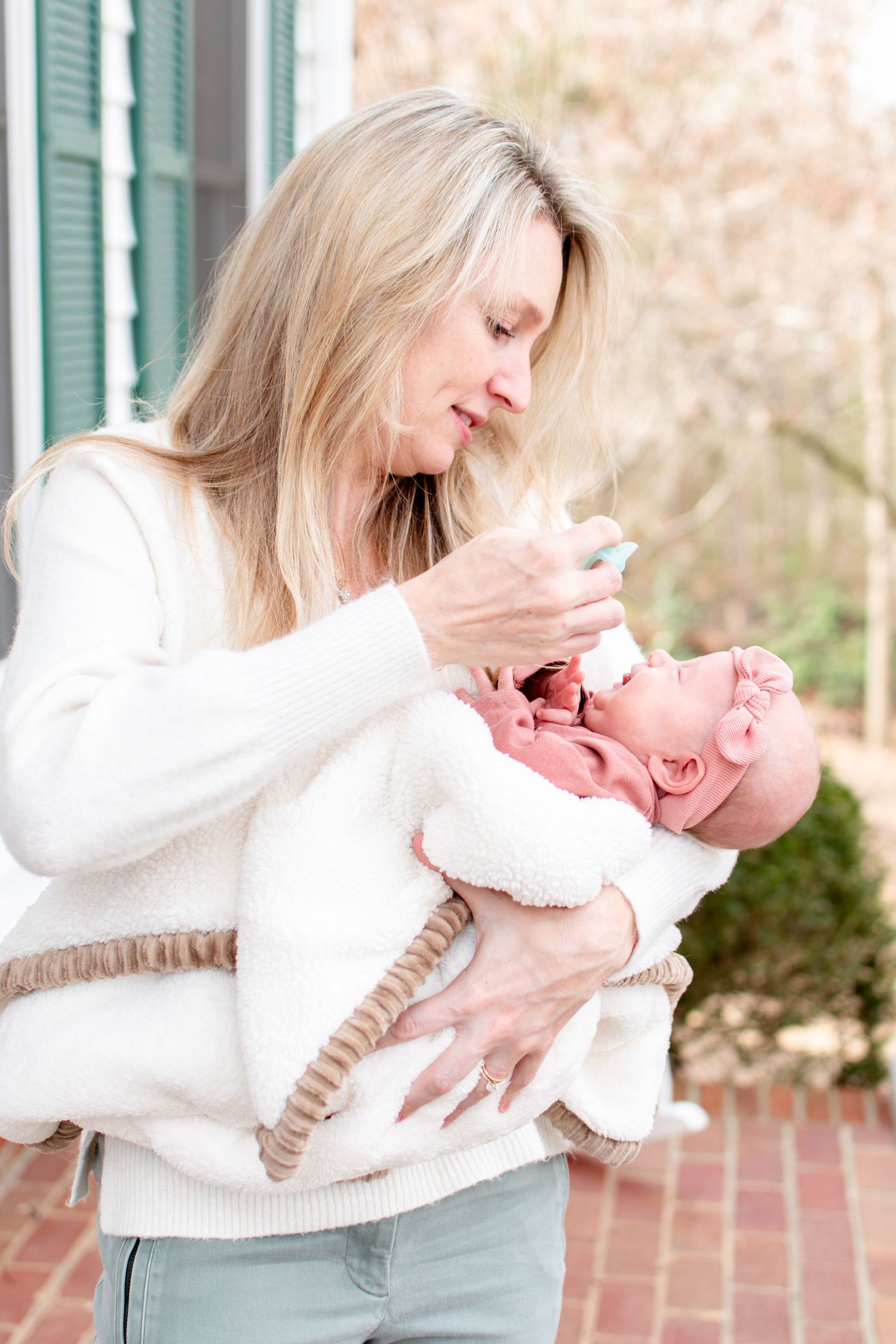 A tender moment between parent and infant outdoors near green shuttered windows.