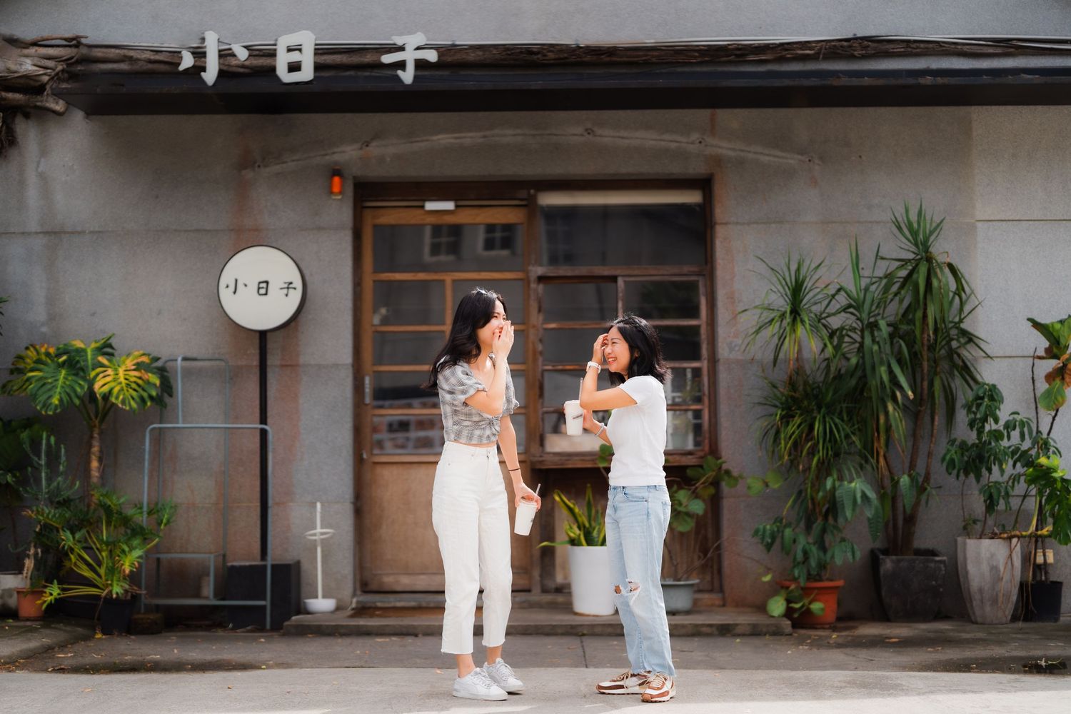 Two people chatting outside a traditional Japanese storefront with potted plants and wooden details.