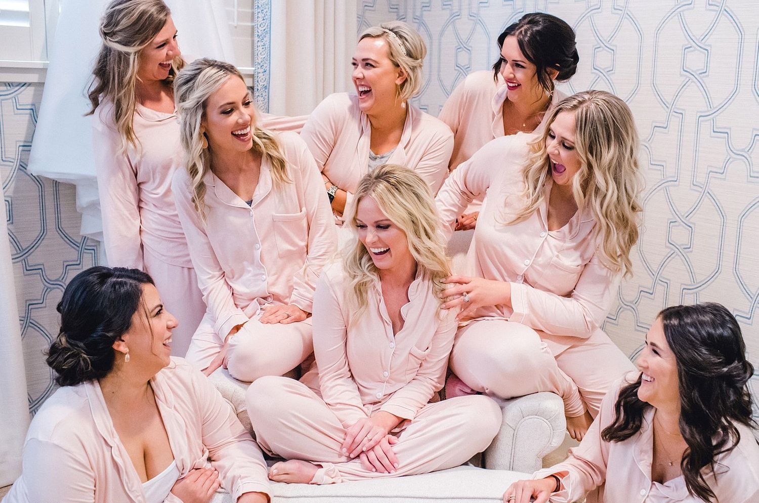 Bridesmaids in matching pink silk pajamas share a joyful moment together during wedding preparations.